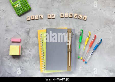Words BACK TO SCHOOL, notebook, pencil, pens and calculator on a gray background. Education or studying concept, flat lay, top view, social media hero Stock Photo