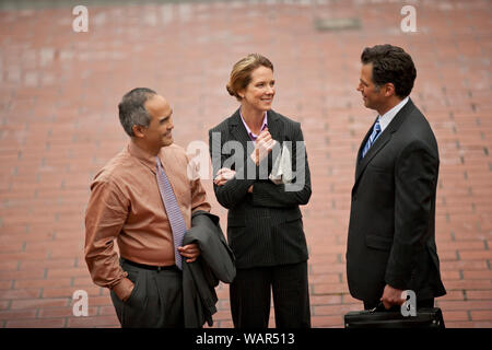 Three business colleagues talking together on a paved sidewalk. Stock Photo