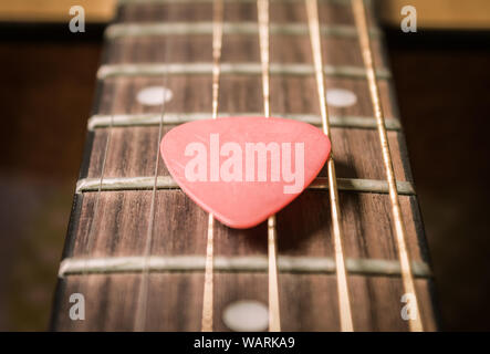 Red Pick on Acoustic Guitar String and Fingerboard or Fretboard in Zoom view Stock Photo