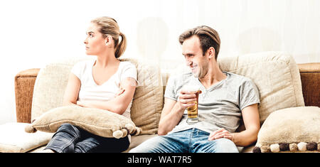 Man drinking beer and his wife is upset. Couple sitting on sofa in home. Stock Photo