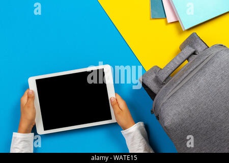 Back to school, education, learning concept. Top view to kid hands with tablet computer, notebooks, books and backpack on colorful background Stock Photo