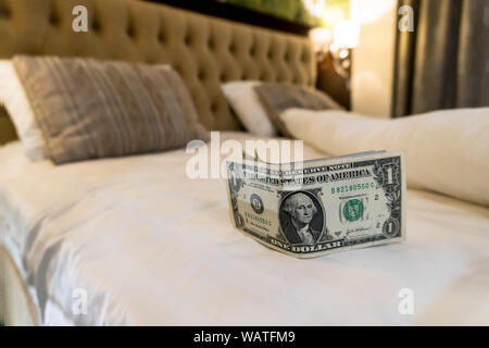 paying us money dollar on white bed in hotel. tips left on the bed for the maid of the hotel room. Tips at the bed for the housekeeper in hotel. Stock Photo