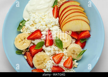Close-up of a blue plate with Healthy dessert with cream, with strawberries, apples and cottage cheese on a white tablecloth. overhead view. Cpoy spac Stock Photo