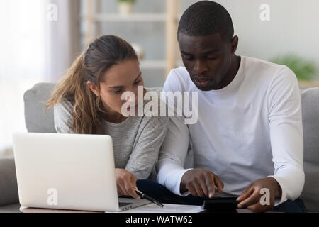 Interracial couple using calculator calculating paying domestic bills do paperwork Stock Photo