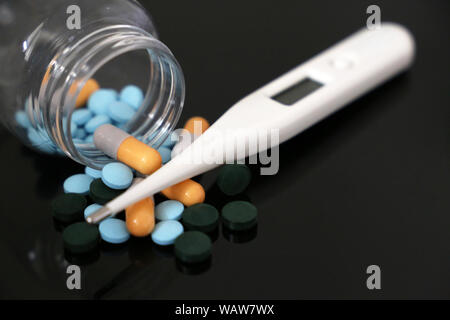 Pills in a bottle, medication in capsules and digital thermometer on a dark glass table. Concept of pharmacy, antipyretic, fever treatment Stock Photo