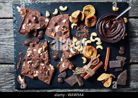 homemade chocolate bar with dried figs and cashew filling on a black stone tray with ingredients, horizontal view from above, flatlay, close-up Stock Photo