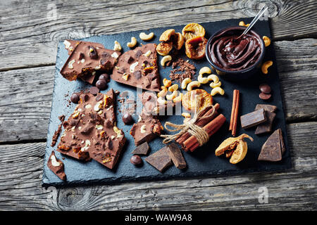 chocolate bar with dried figs and cashew filling broken up on pieces on a black stone tray with ingredients, horizontal view from above, close-up Stock Photo