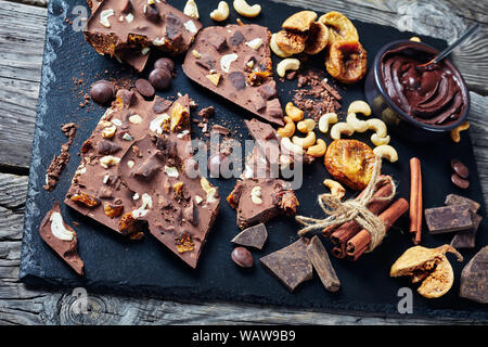 homemade sweet milk chocolate bar with dried figs and cashew filling on pieces on a black slate tray with ingredients, horizontal view from above, Stock Photo