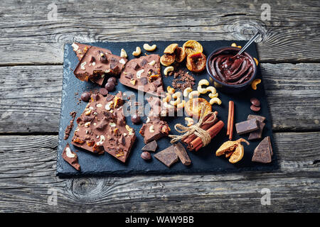 homemade chocolate bar with dried figs and cashew filling broken up on pieces on a black stone tray with ingredients, horizontal view from above,close Stock Photo