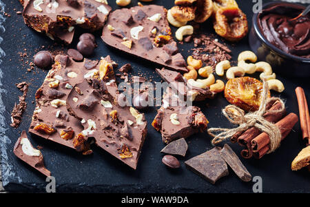 delicious sweet chocolate bar with dried figs and cashew filling on pieces on a black slate tray with ingredients, view from above, close-up Stock Photo