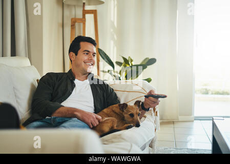 Relaxed man lying with his dog on sofa watching tv in living roo Stock Photo
