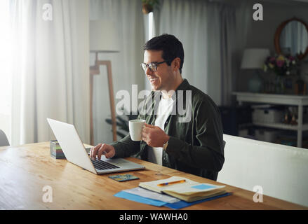 Smiling man enjoying the coffee while using laptop at home Stock Photo