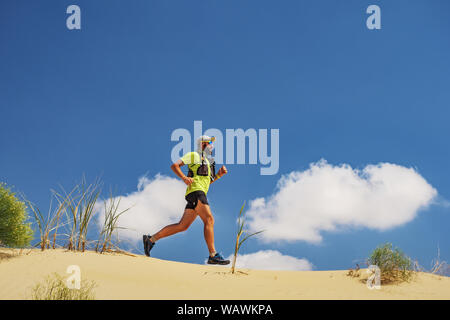 Athlete runs along the sandy desert. Desert trail running. A man in shorts and a T-shirt is running through the sandy wilderness. Stock Photo