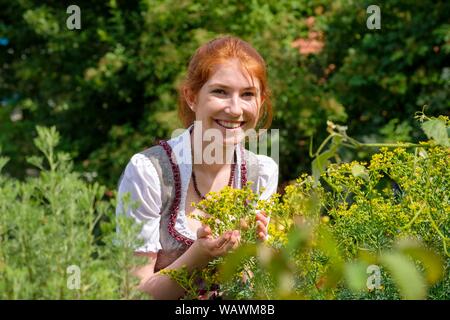 Young woman smells on herbs, in the herb garden, Upper Bavaria, Germany Stock Photo