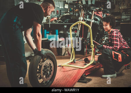Mechanic and his helper repairing a motorcycle in a workshop. Stock Photo