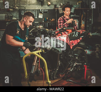 Mechanic and his helper repairing a motorcycle in a workshop. Stock Photo