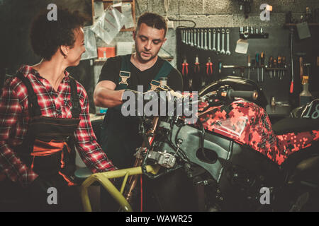 Mechanic and his helper repairing a motorcycle in a workshop. Stock Photo