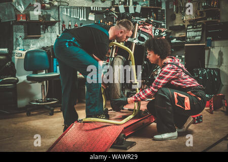 Mechanic and his helper repairing a motorcycle in a workshop. Stock Photo