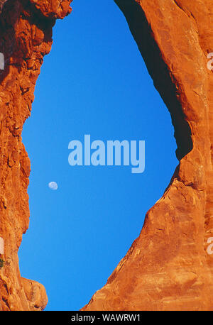 USA. Utah. Arches National Park. The moon viewed through a hole in sandstone rock formation. Stock Photo