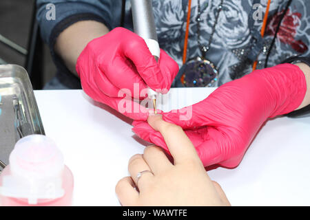 Hardware manicure. Finger treatment of nails. Electric nail file in action. Closeup of the hands of a beautician in red gloves. The master removes the Stock Photo