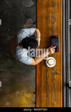 Asian young man using tablet while having hot cappuccino Stock Photo