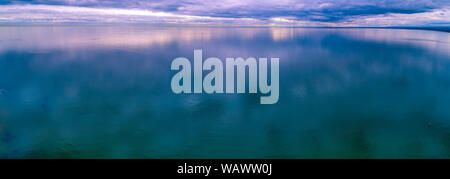 Storm low clouds reflecting in smooth and calm ocean water - aerial panoramic seascape Stock Photo