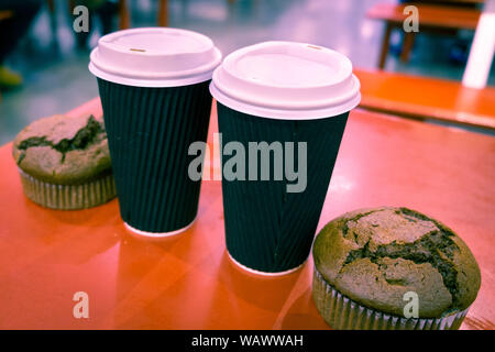 Two disposable coffee cups with two chocolate muffins on red table with shallow focus Stock Photo