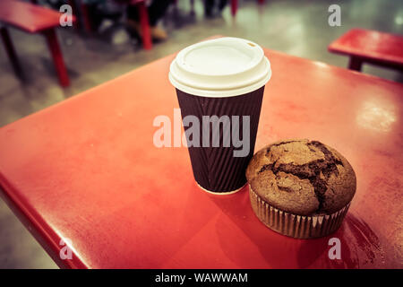 Closeup of chocolate muffin and disposable tall coffee cup placed on red table Stock Photo