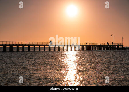Couple walking their dog on a pier silhouettes at sunset Stock Photo