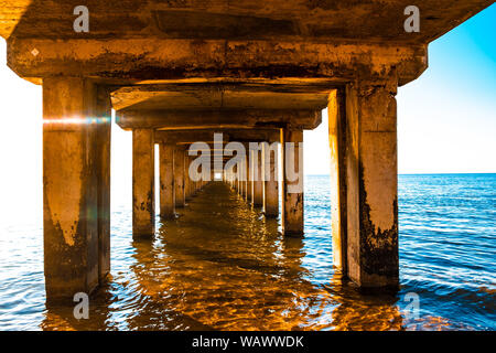 Diminishing perspective of wooden pillars underneath long old pier standing in ocean water at sunset