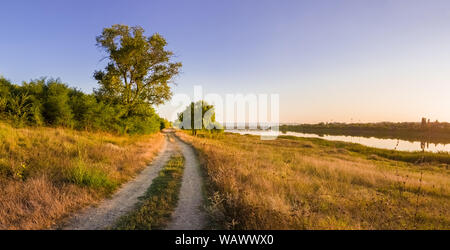 Scenic countryside landscape with rural dirt road across a meadow with dry grass and hay under a clear blue sky. Autumn panorama view near Delia lake, Stock Photo