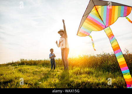 Father with son launching colorful air kite on the field during the sunset. Concept of a happy family having fun during the summer activity Stock Photo