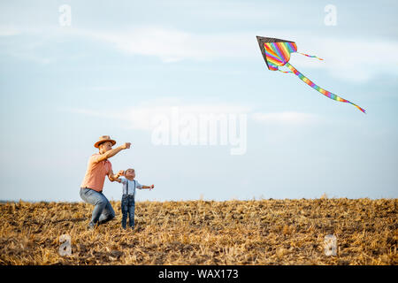 Father with son launching colorful air kite on the field. Concept of a happy family having fun during the summer activity Stock Photo