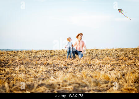 Father with son launching colorful air kite on the field. Concept of a happy family having fun during the summer activity Stock Photo