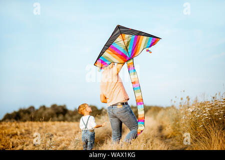 Father and son walking together with colorful air kite on the field, back view. Concept of a happy family during the summer activity Stock Photo