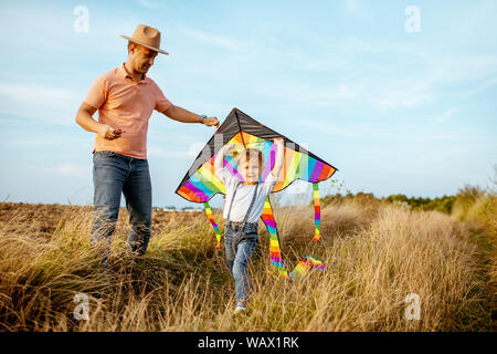 Father with son launching colorful air kite on the field. Concept of a happy family having fun during the summer activity Stock Photo