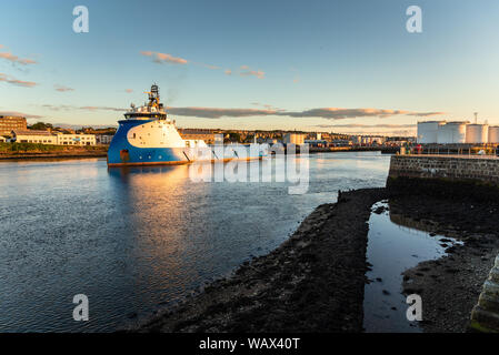 Platform supply ship leaving a harbour with fuel tanks on the piers at sunset Stock Photo