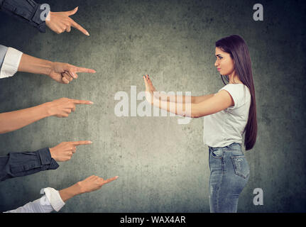 Confident woman keeping hands in stop gesture, defending herself from blaming  people with pointing fingers at her Stock Photo