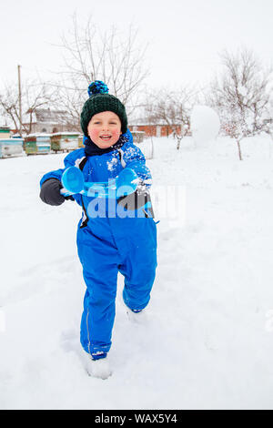 Happy boy sculpts and throws snowballs. Winter games in the fresh air. Winter vacation. Stock Photo