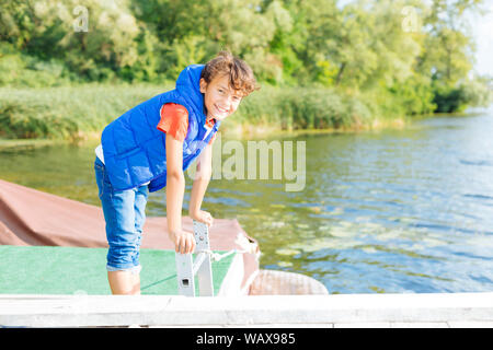 Beaming dark-haired boy smiling while standing near lake Stock Photo