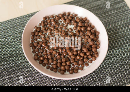 Chocolate cereal balls with milk in a bowl on napkin on wooden table. Dry breakfast cereal balls. Healthy breakfast concept. Stock Photo