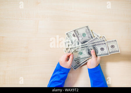 Top view, close-up of hands counting money. Happy child with money dollar, little businessman. Pile of United States dollar hundred USD banknotes in b Stock Photo