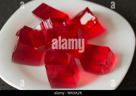 Red jelly cubes on white plate background. Berry sweet pieces of jelly. Homemade red cherry gelatin dessert. Stock Photo