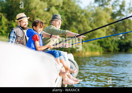 Boy feeling happy while fishing with father and grandfather Stock Photo