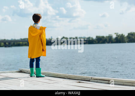Dark-haired boy wearing yellow raincoat and wellingtons Stock Photo