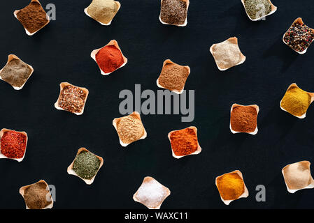 Variety of spices and herbs in bowls, a pattern on a black background. Flat lay of condiments background. Above view with flavors. Cooking frame. Stock Photo