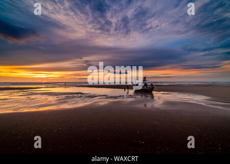 Beautiful sunrise over an old wooden fishing boat on a pebble beach