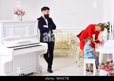 Home schooling concept. Kid growthing in welfare. Parents enjoying parenthood, happy. Father stands near piano, watching while mother teaches son pres Stock Photo