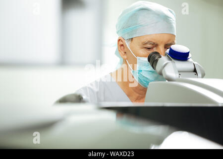 Smart mature doctor sitting in front of the microscope Stock Photo