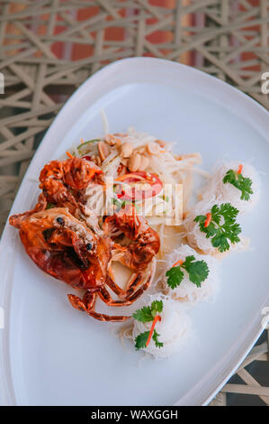 Som Tum - Thai spicy papaya salad with deep fried soft shell crab and rice noodle in white plate. Top view Stock Photo